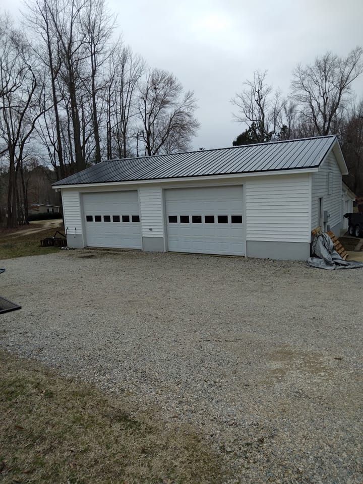 White three-car garage with gray roof and gravel driveway in a leafless yard