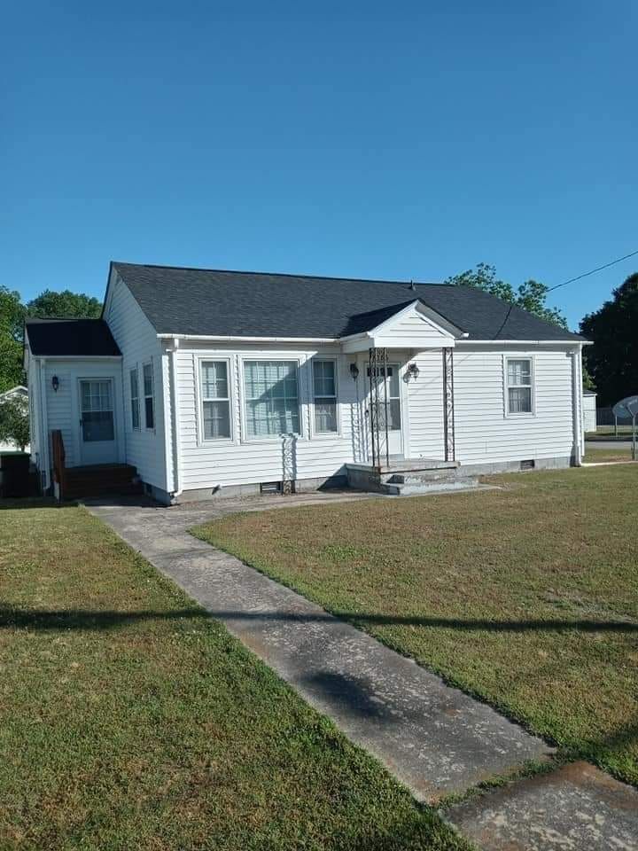 Small white single-story house with a front porch and a concrete walkway in a sunny yard.