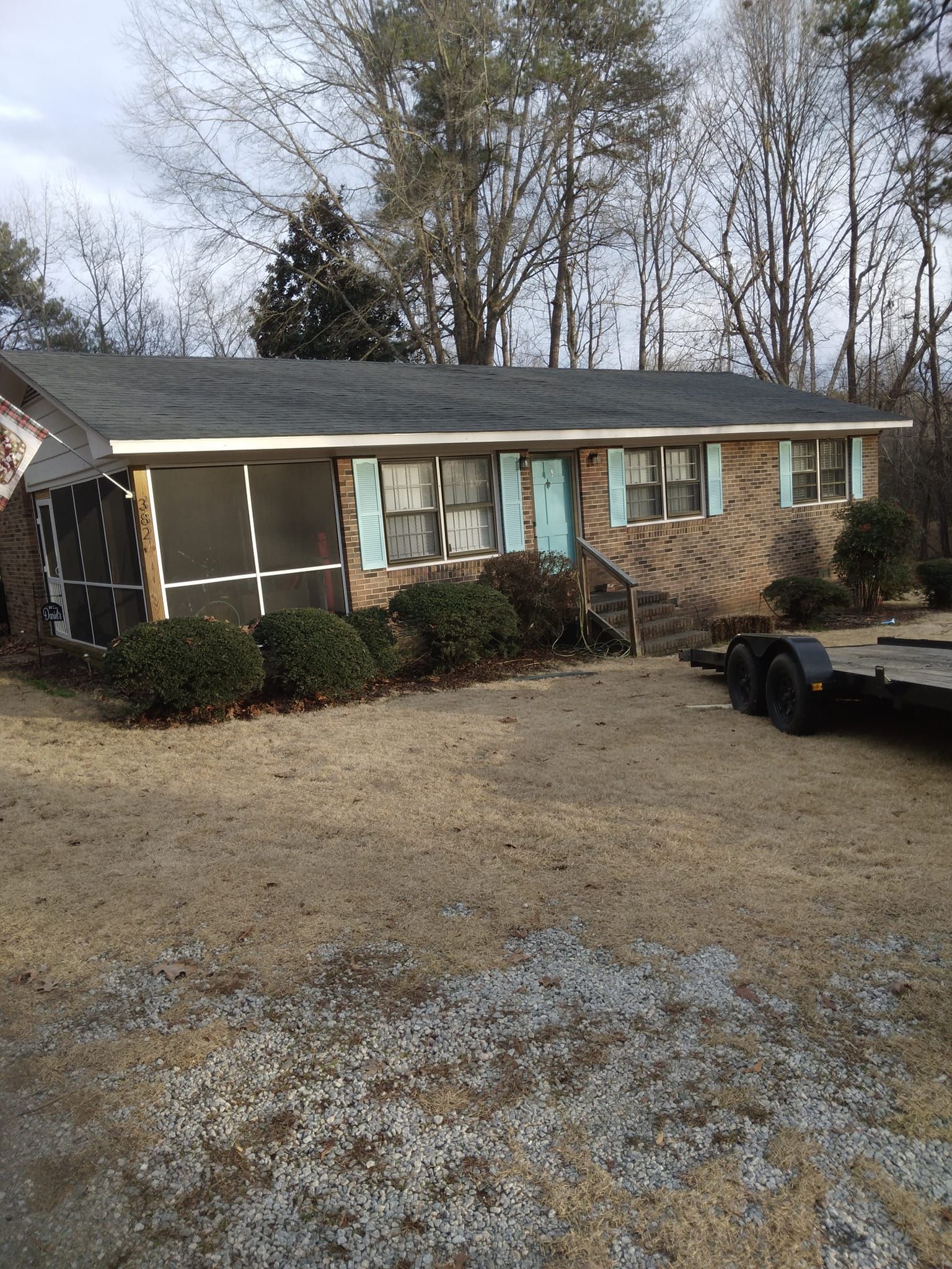 Single-story brick house with a gravel driveway and trees in the background