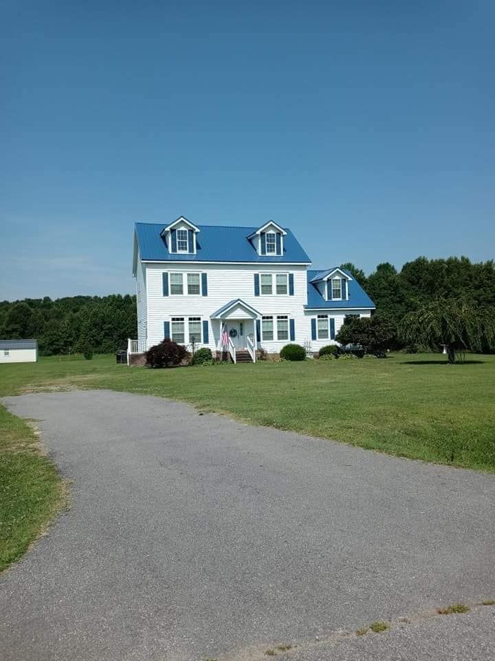 White house with blue roof and shutters beside a curved driveway under a clear blue sky