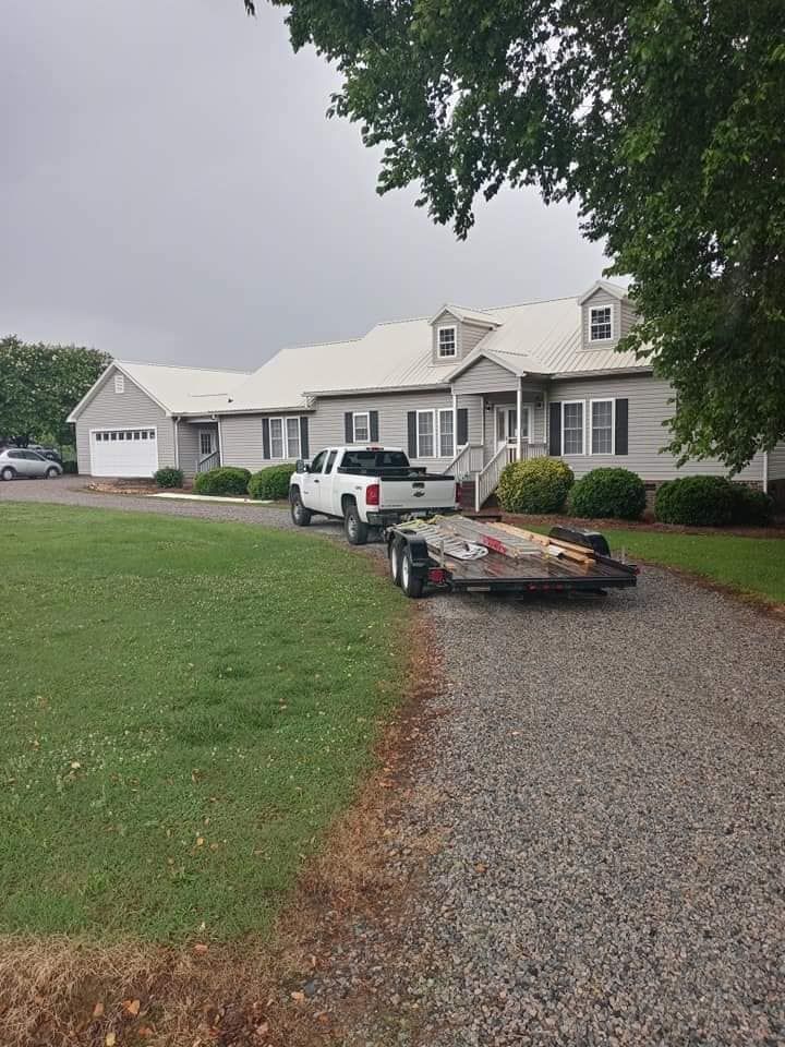 White house with a gravel driveway, parked SUV, and flatbed trailer under cloudy skies.