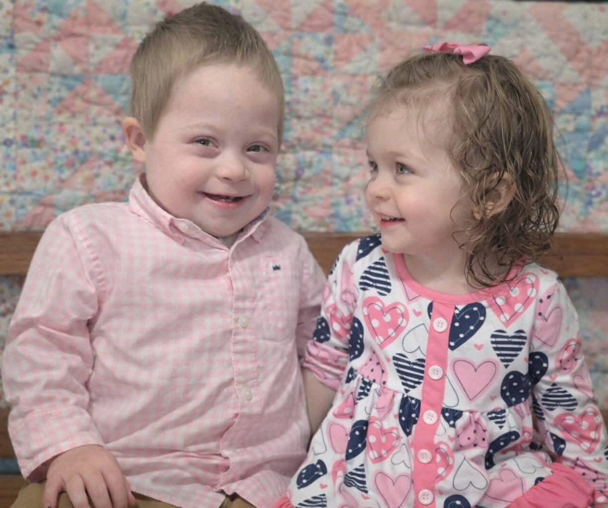 Two smiling toddlers sitting side by side in pastel clothes against a patterned backdrop