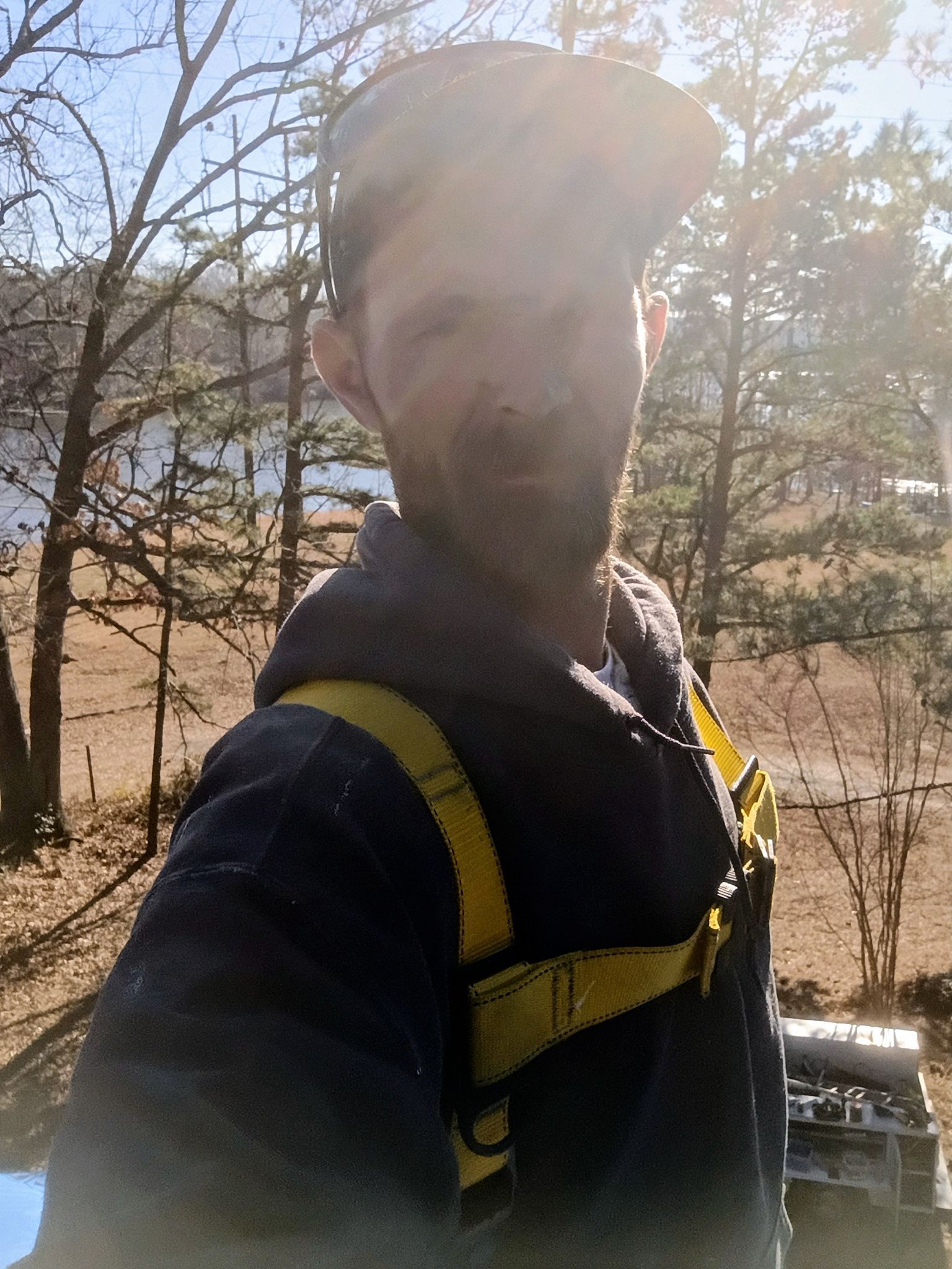 Person wearing a yellow backpack in a sunny wooded area, taking a selfie outdoors