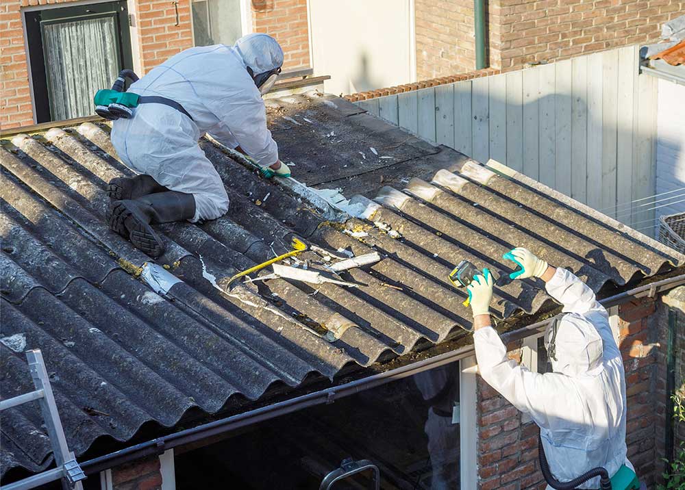 Two workers in protective suits clean a corrugated roof on a building.