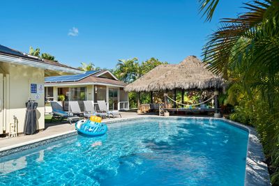 A swimming pool in front of a patio and a thatched-roof cabana on a bright, sunny day.