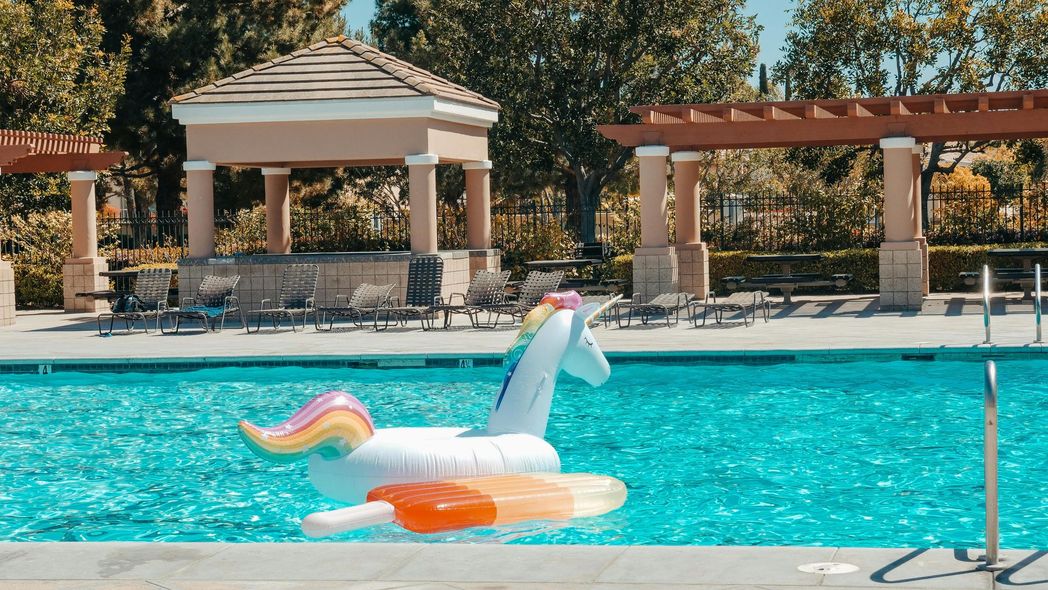 A white inflatable unicorn float with a rainbow tail and orange wings floating in a bright blue swimming pool.