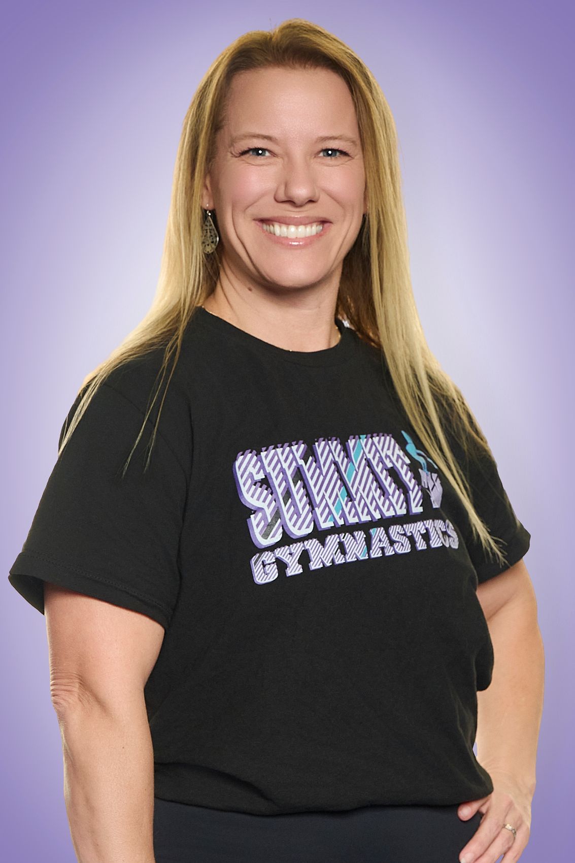 Woman in black T-shirt with purple logo, smiling against a purple background.