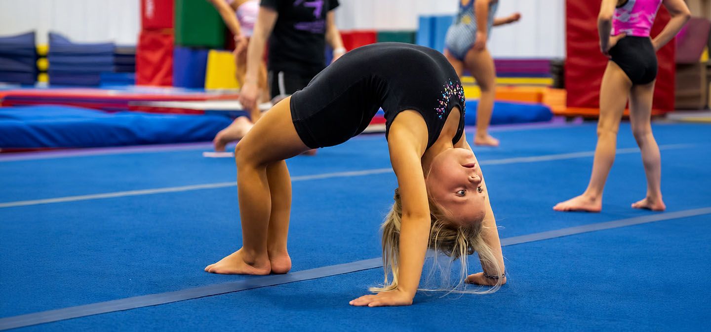 Young gymnast in a backbend on a blue mat in a gymnastics gym