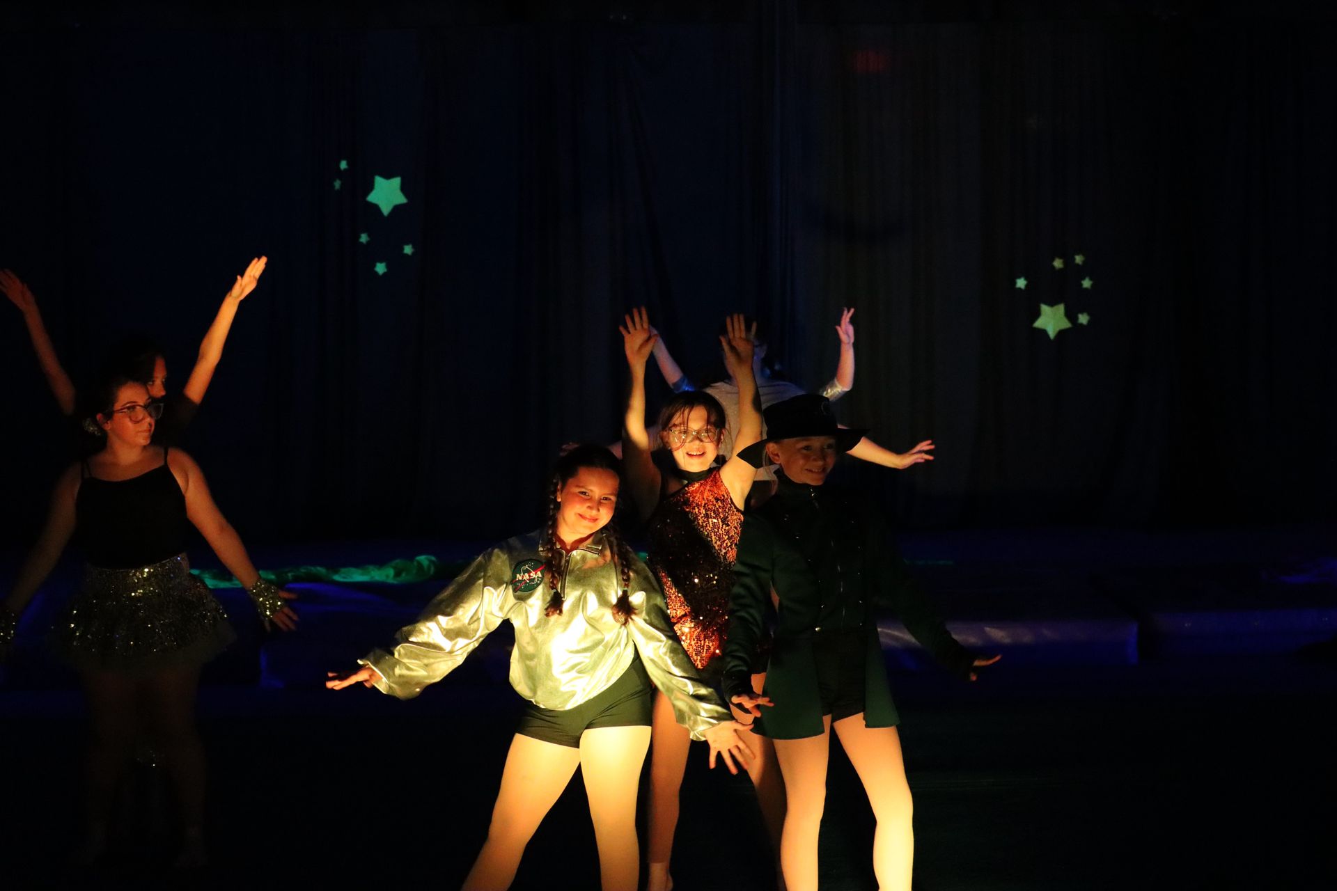 Four dancers in colorful costumes posing on a dim stage with arms raised