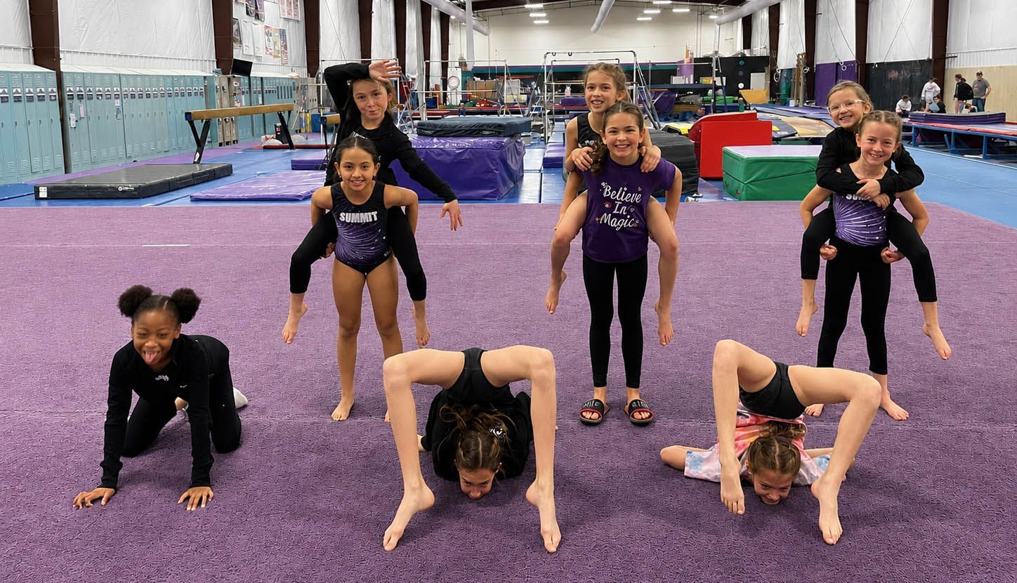 Children doing gymnastics on purple mats in a gym, posing and stretching in a group.