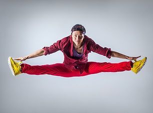 Person in a red tracksuit doing a wide mid-air split against a light gray background