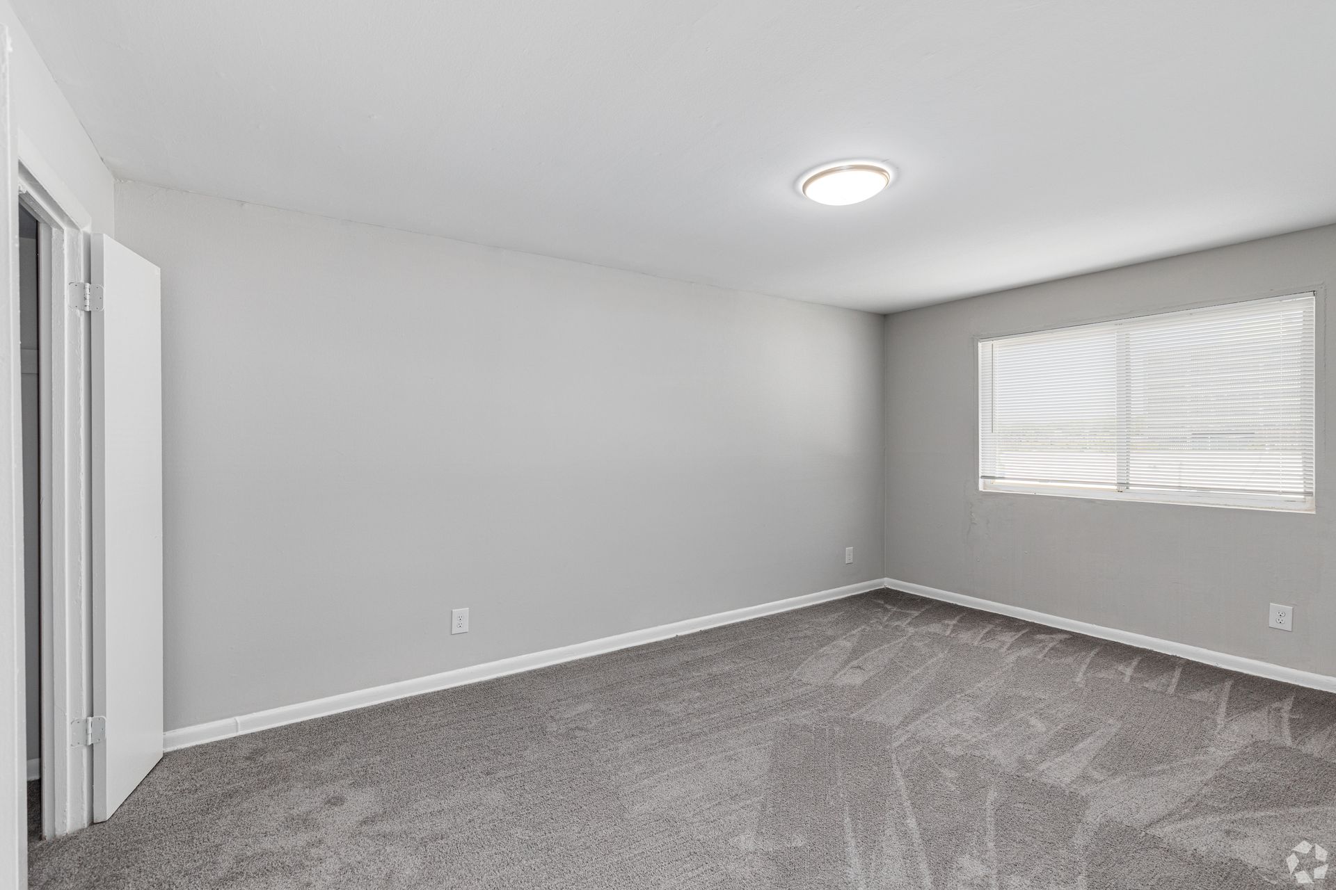 An empty bedroom with a carpeted floor and a window.