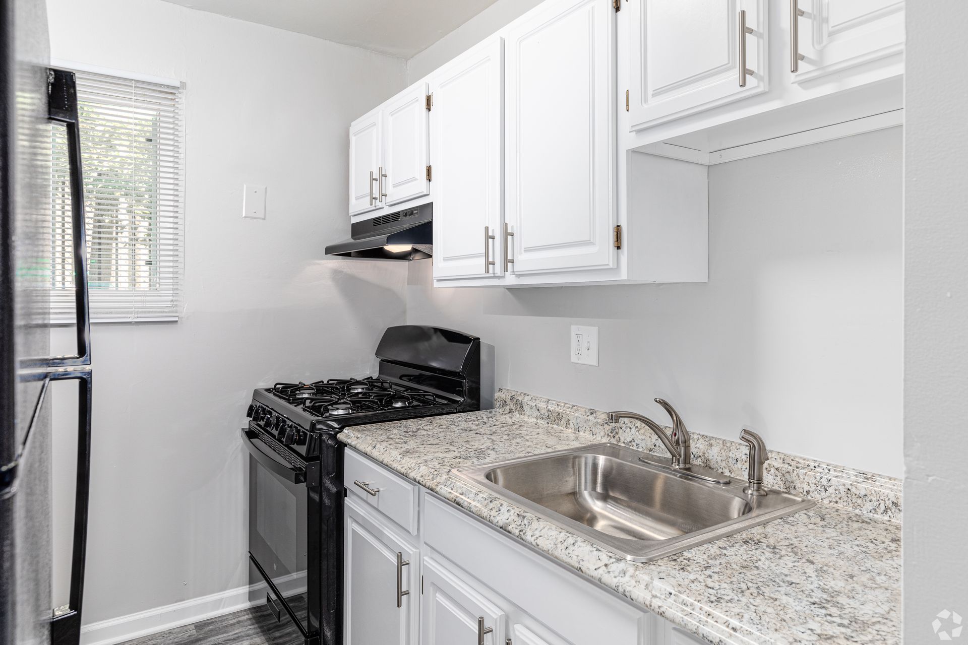 A kitchen with white cabinets , a stove , a sink , and a refrigerator.