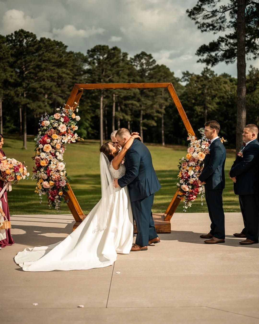 bride and groom kissing under wooden arch during outdoor wedding ceremony