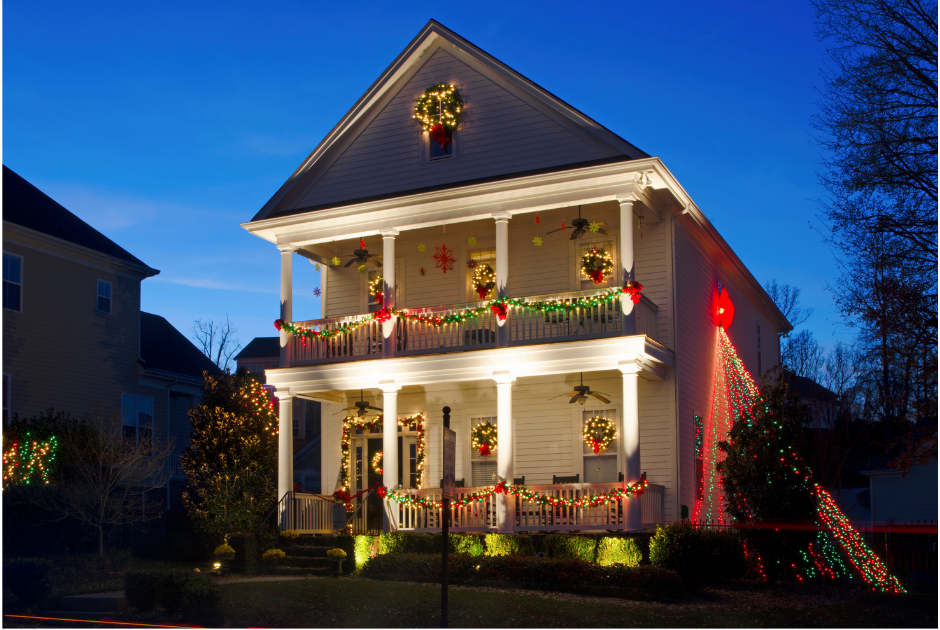 Two-story white house decorated with Christmas lights and wreaths, lit up at dusk.