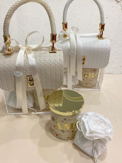 Due borse bianche intrecciate con dettagli dorati e scatole regalo decorative abbinate su una superficie bianca