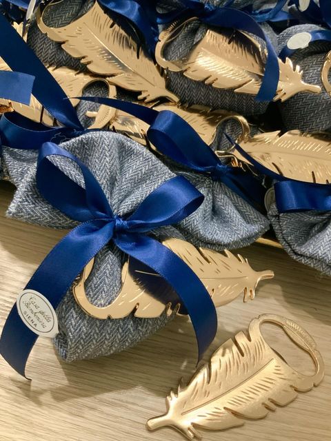Scatoline portaconfetti a forma di foglia, in argento e oro, legate con un nastro blu su un tavolo.