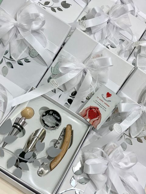 Scatole regalo argentate, legate con nastri bianchi, contenenti un vassoio con un assortimento di trucchi e accessori.
