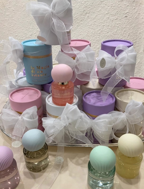 Scatole regalo color pastello e piccole bottiglie avvolte con fiocchi bianchi, disposte su un tavolo.