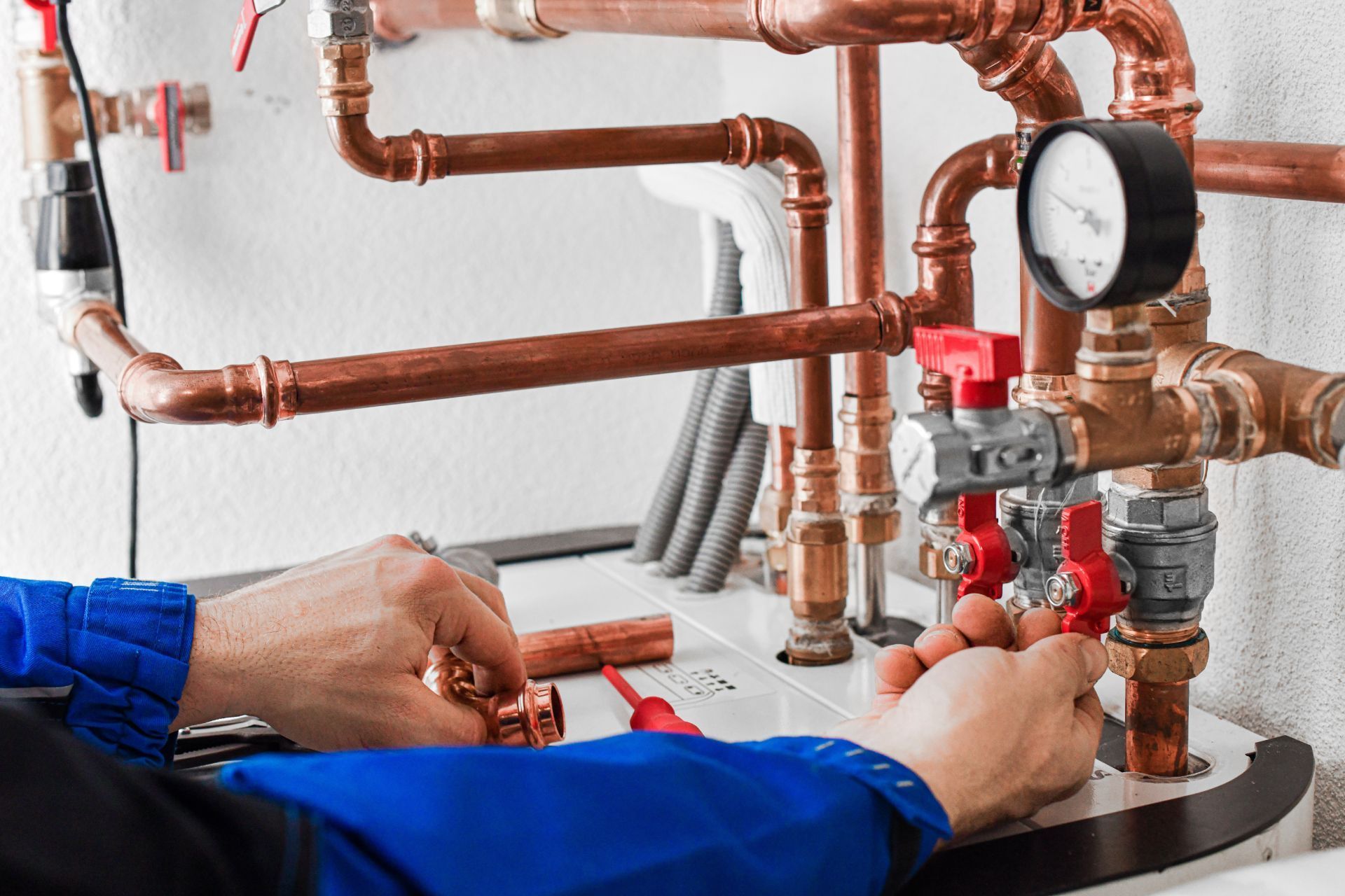 Plumber adjusting valves on copper pipes and pressure gauge in a boiler room