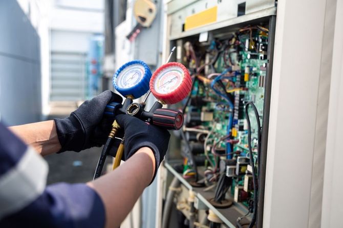 HVAC technician using gauges to service an air conditioning unit on a rooftop.