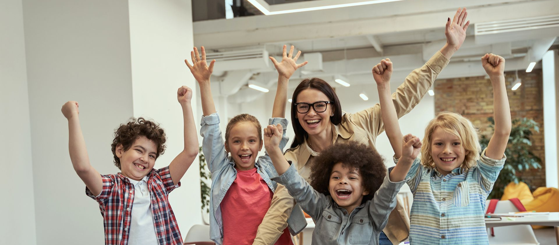 Children and teacher smiling with arms raised in a bright classroom