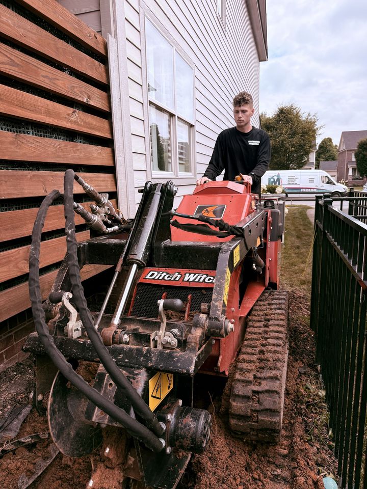 Person on a red tracked machine beside a house, clearing debris near a fence.