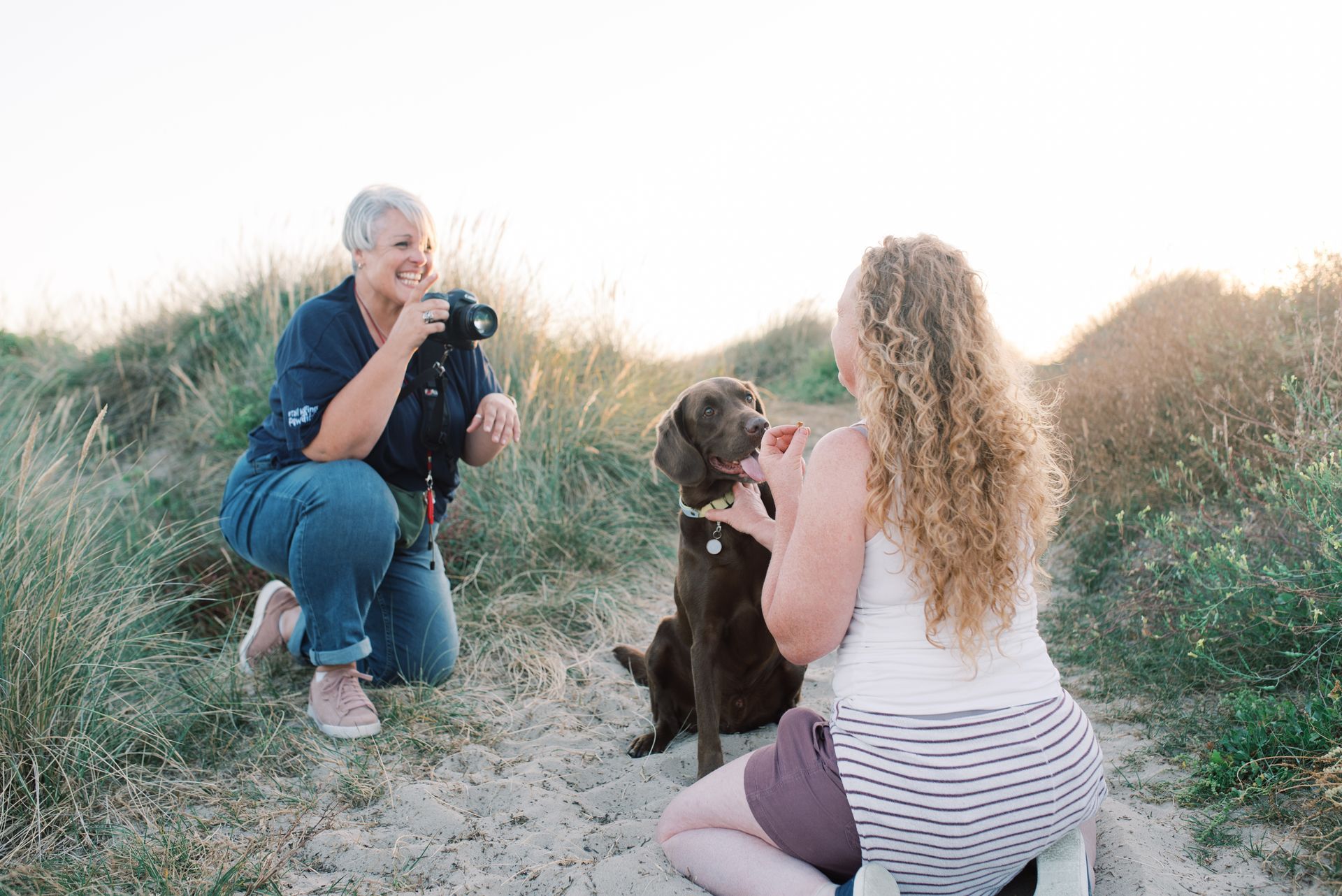 professional dog photographer taking a photo of a dog and their human on the beach .