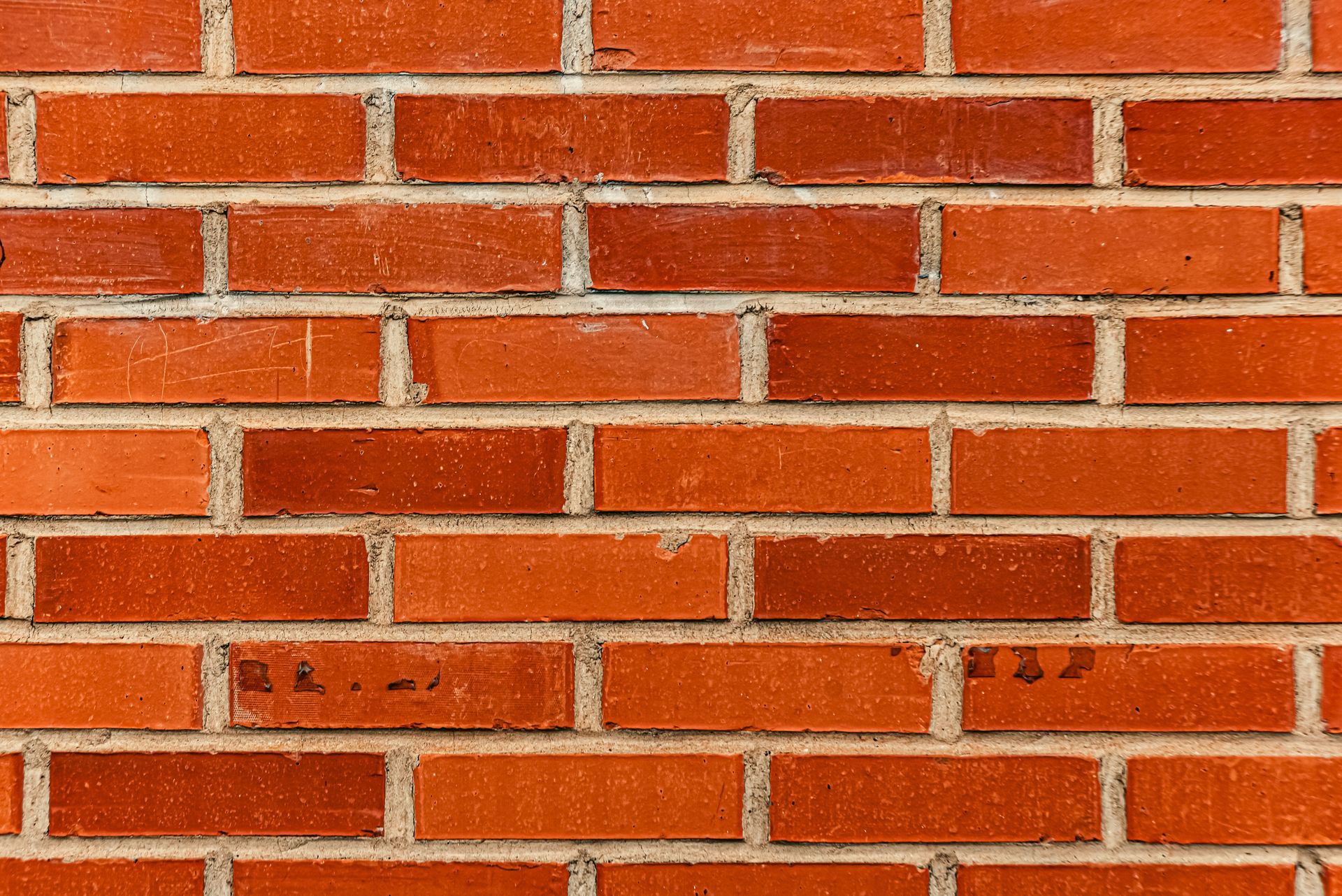 A full-frame view of a wall featuring a repeating, uniform pattern of orange-red bricks laid in a standard running bond.