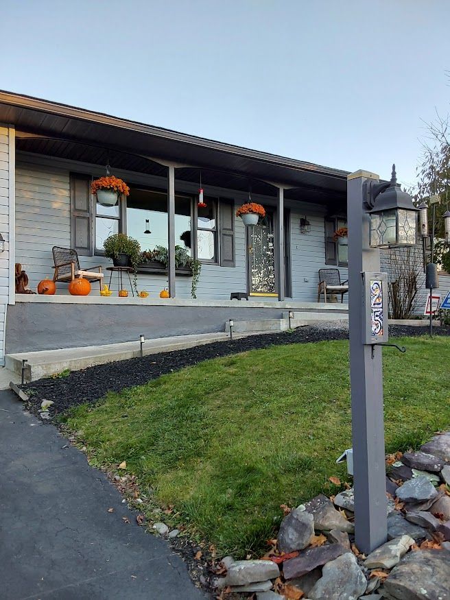 A light blue brick home with pumpkins, flowers, and a dark gray mailbox.
