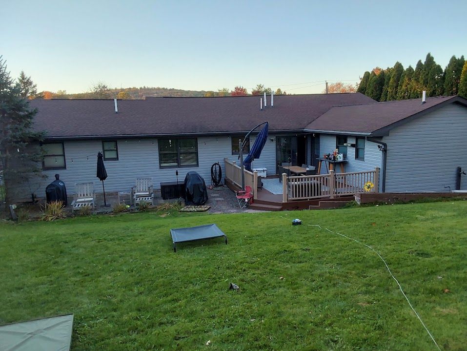 Backyard view of a house with a deck, lawn, and trees. The siding is gray.