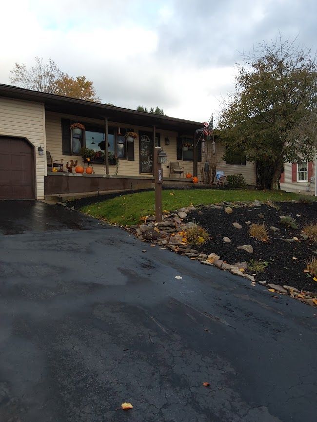 Ranch house with pumpkins and fall decorations. Asphalt driveway and landscaped front yard. Overcast sky.