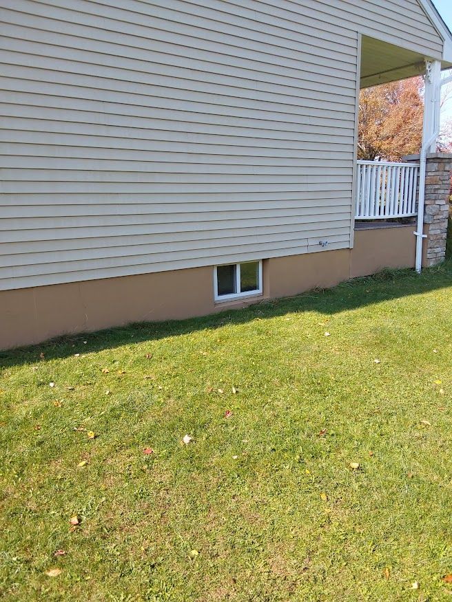 Tan house with beige siding and brown foundation, small window, and green grass.