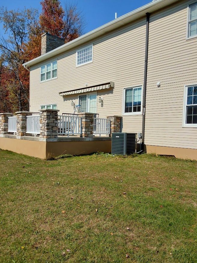 Back of a beige house with a deck. Deck has stone pillars and white railings. AC unit on the ground.