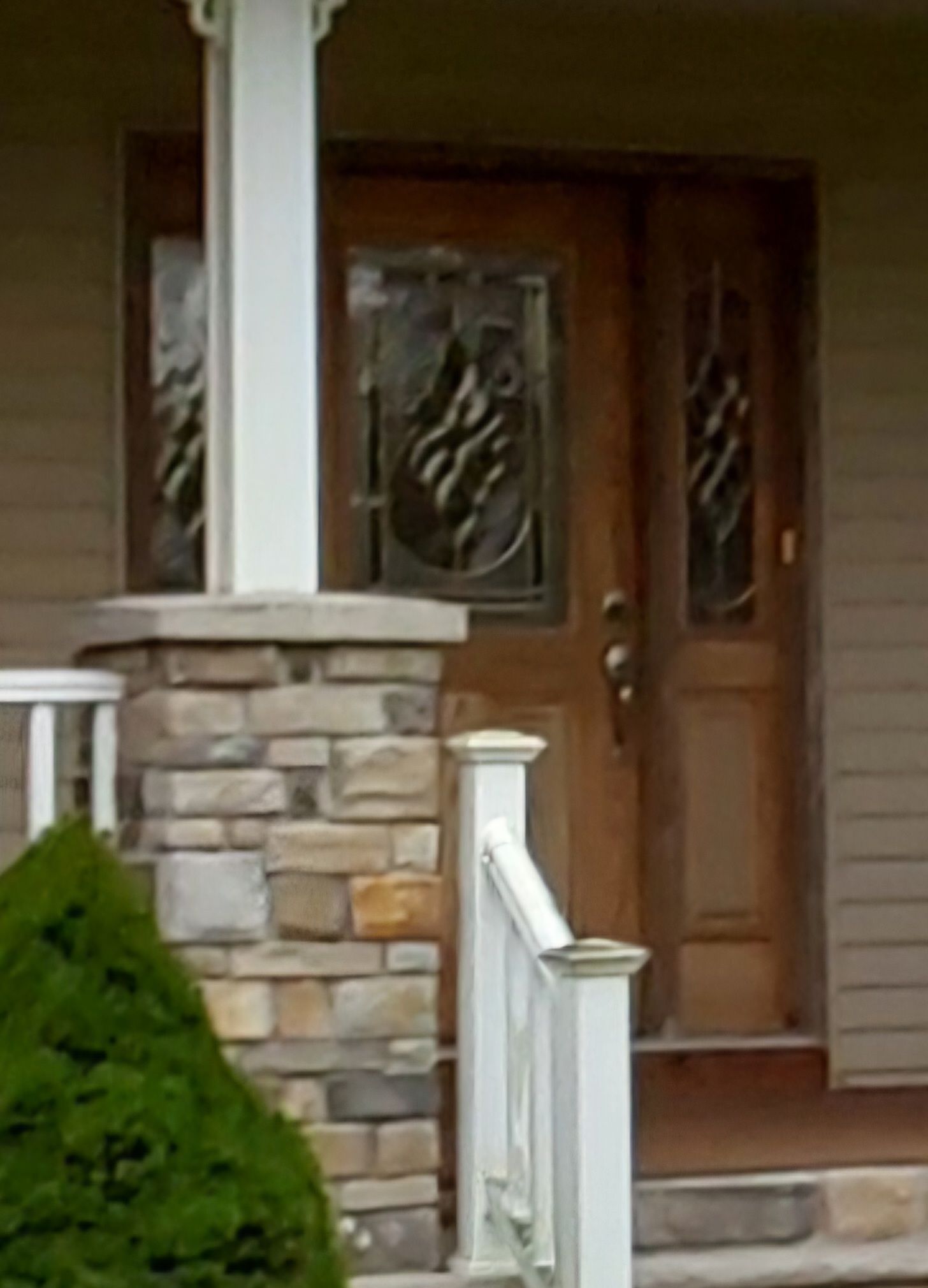 Wooden double doors with decorative glass panels, fronted by a stone pillar and white railing.