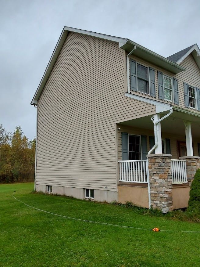 Beige two-story house with green shutters, a porch, and a grassy yard under a cloudy sky.