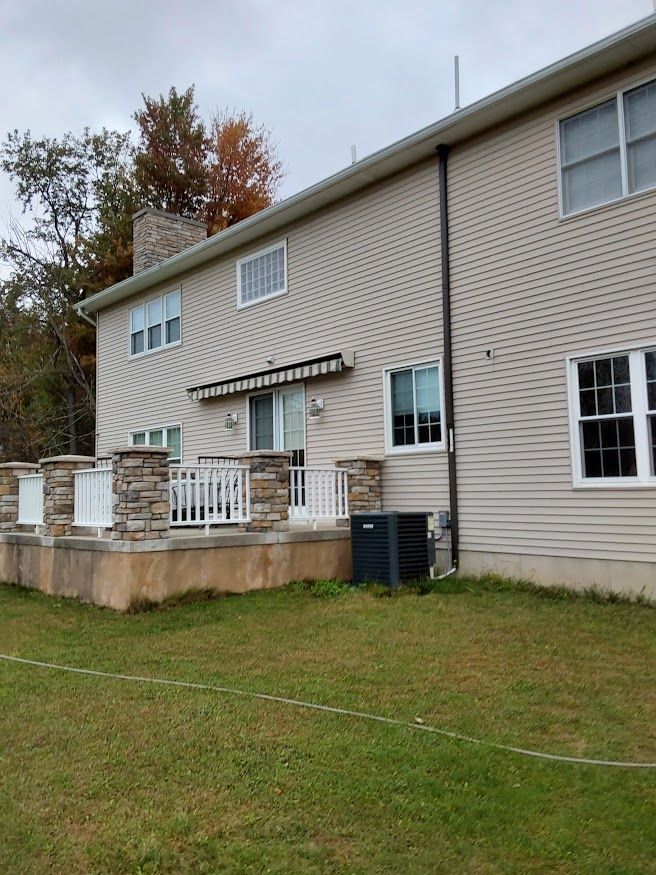 Back of a two-story house with a deck. Beige siding, white trim, and stone columns, set in a grassy yard.