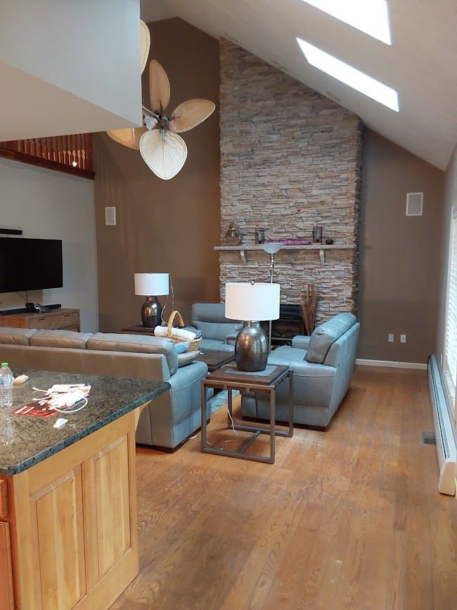 Living room with stone fireplace, gray couches, wooden floor, and fan.