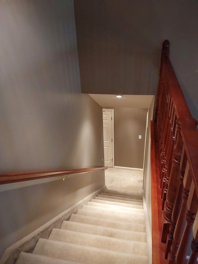 Staircase leading down to a hallway, with a wooden railing and carpeted steps. Gray walls.