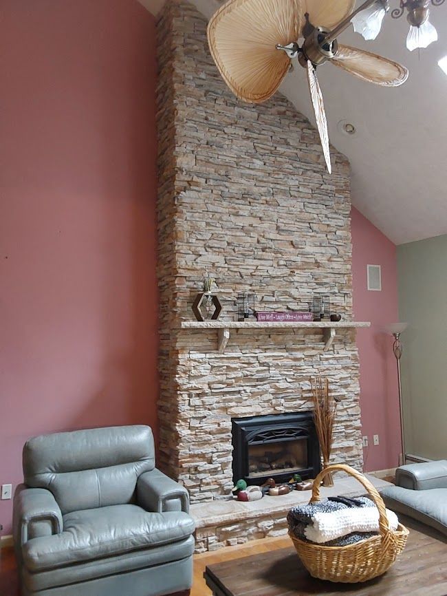 Stone fireplace in a pink room, with a leather armchair, basket, and ceiling fan.