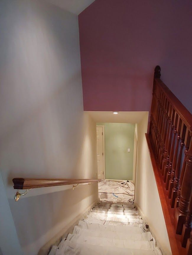 Staircase with wooden banister and a doorway at the bottom. Walls are painted pink and white.