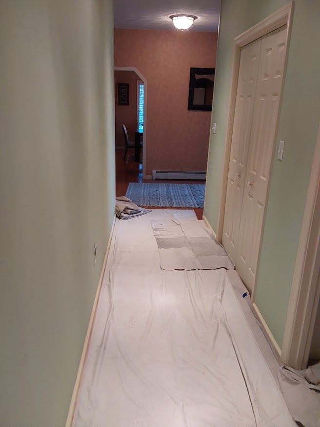 Narrow hallway with new marble-like tile partially installed; light green walls, white door, and a view into another room.