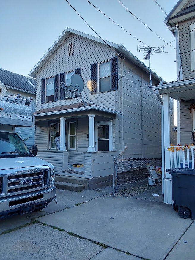 Two-story house with light siding, black shutters, small porch. A parked van is in front.