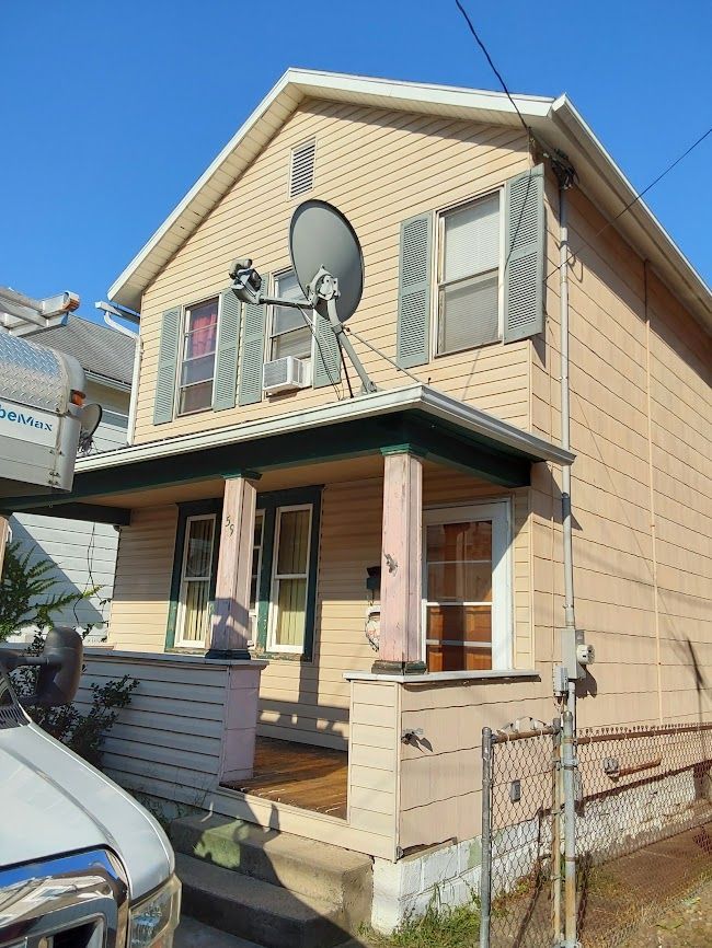Two-story tan house with green trim, pink pillars, and satellite dishes on the second floor.