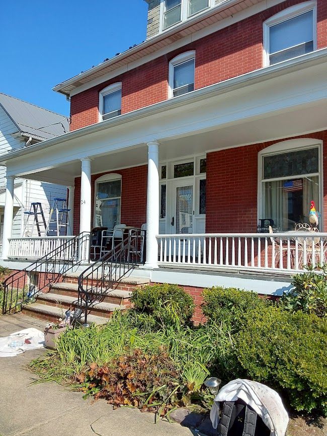 Red brick house with a white porch, stairs, and front garden under a blue sky.