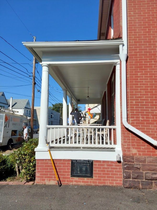 A brick house with a white porch, columns, and railing. People are on the porch.