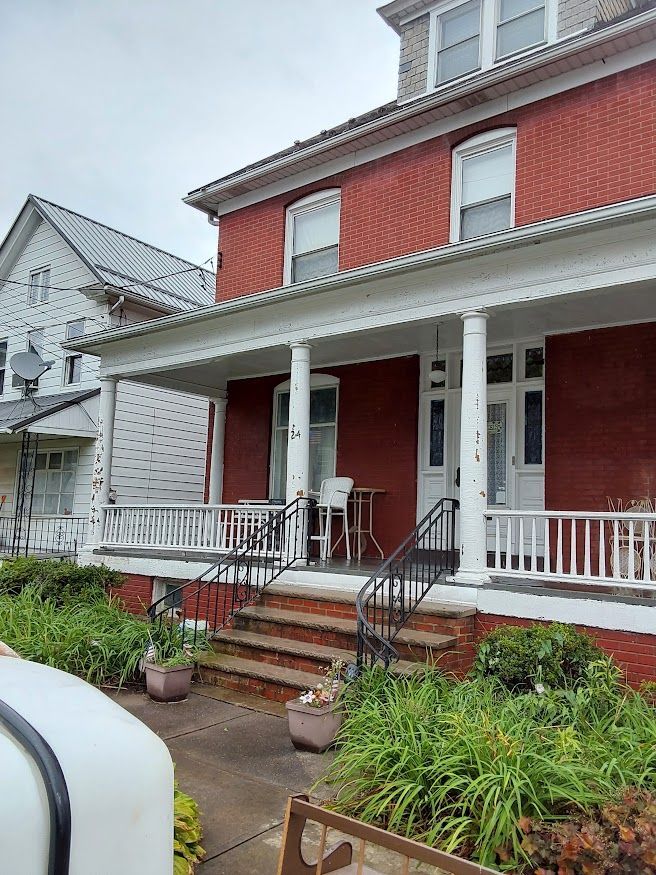 Red brick house with a white porch, front steps, and a white house next door.