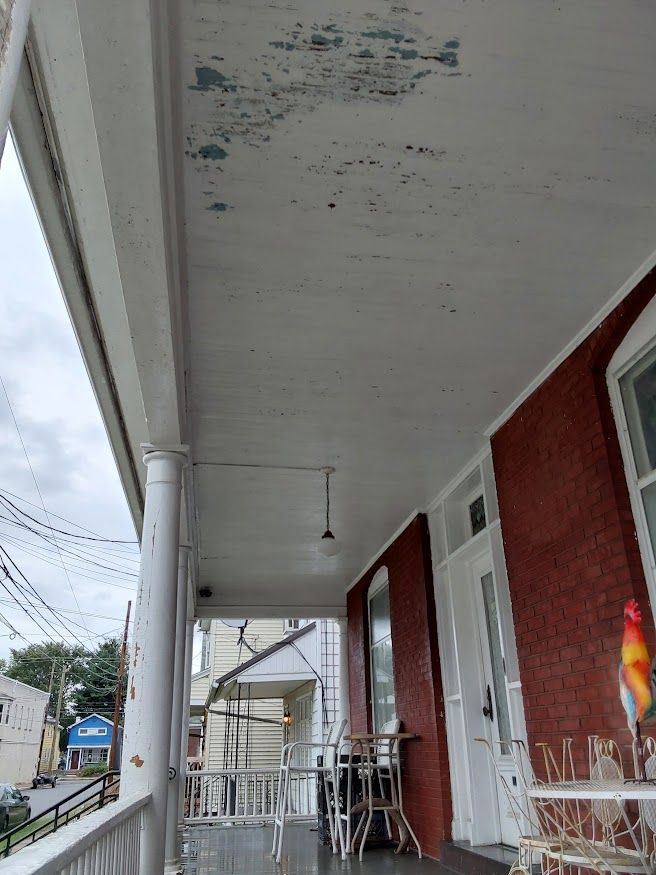 Porch ceiling with peeling paint, over a brick building, on a cloudy day.