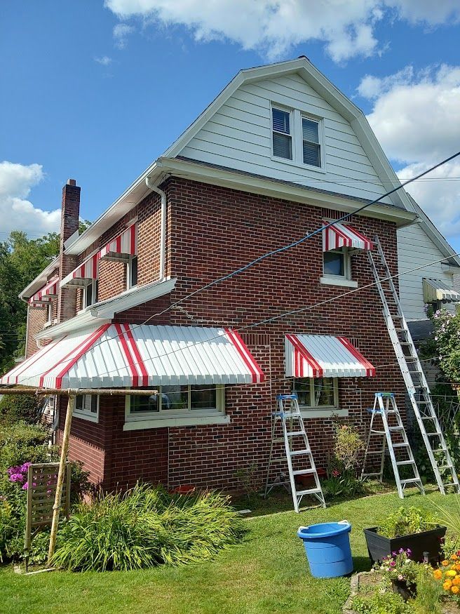 Brick house with red and white awnings, two ladders. Blue sky, sunny day.