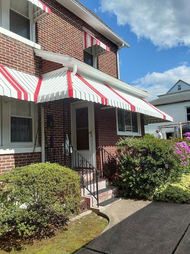Brick building with red and white striped awnings over windows and door. Green bushes and a sidewalk in front.
